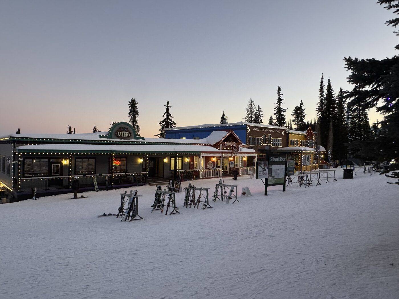 Colourful alpine village storefronts at SilverStar lit up with string lights at dusk